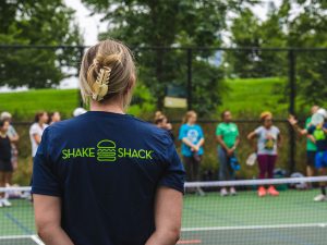 Woman with Shake Shack tshirt facing a pickleball court.
