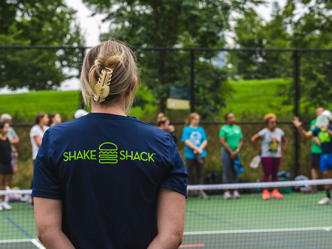 Woman with Shake Shack tshirt facing a pickleball court.