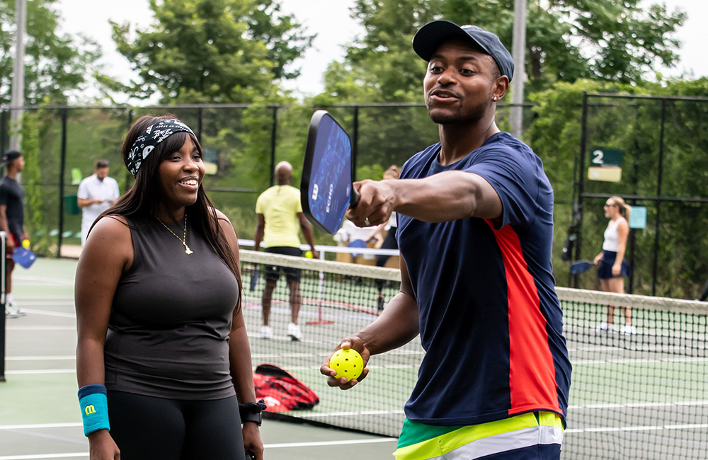 Coach Chris Clark teaching pickleball to young, black woman.